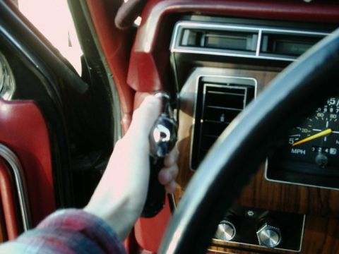 1984 Ford Bronco - Hand turns ignition key in the interior of a 1984 Ford Bronco, revealing dashboard details and gauges.