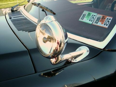 1984 Ford Bronco - Close-up of a black vehicle's fender, showing a chrome side mirror and windshield wipers, with registration stickers on the windshield.