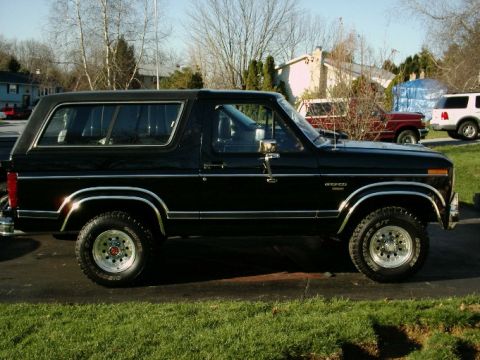 1984 Ford Bronco - This black Ford Bronco is parked in a residential area with other vehicles visible in the background.