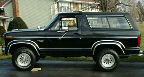 1984 Ford Bronco - Side profile of a black Ford Bronco SUV with chrome accents and aftermarket wheels.