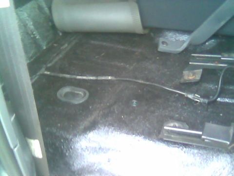 1992 Ford Bronco - The image shows the interior floor of a vehicle, revealing seat mounting hardware and a visible cable running across the carpeted surface.