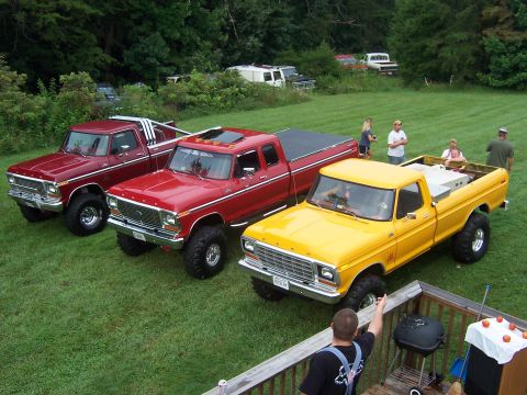 1978 Ford Bronco - Three lifted Ford pickup trucks are parked on a grassy lawn, with people standing around them.