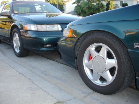 1995 Ford Taurus - Two dark green sedans are parked side-by-side on a street.