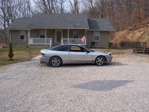 1996 Ford Probe - A silver coupe is parked in a gravel driveway in front of a house.