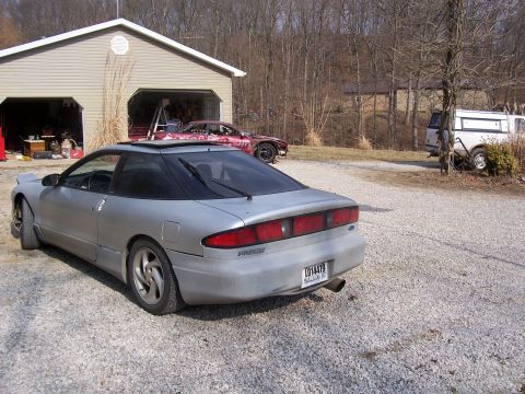 1996 Ford Probe - A silver coupe is parked in a gravel driveway next to a garage, with another vehicle visible inside.