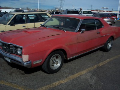 1972 Ford Ranchero - A red coupe with a hood scoop is parked in a lot next to another vehicle.