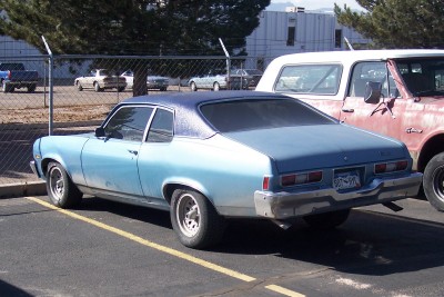 1972 Ford Ranchero - This light blue coupe, likely a 1975 model, is parked next to a red truck. The license plate is visible.