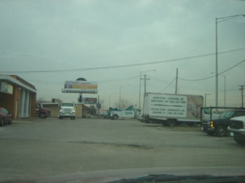1992 Ford Bronco - Several trucks are parked in a lot under an overcast sky, with a billboard visible.