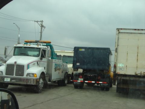 1992 Ford Bronco - A tow truck and a dump truck are parked side-by-side under a cloudy sky.
