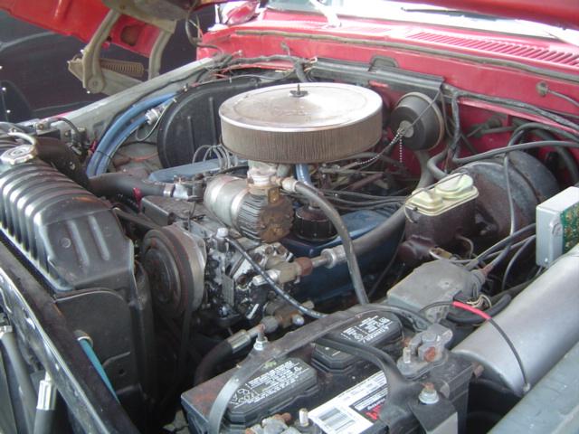 Engine bay with V8 engine, radiator, battery, and brake fluid reservoir visible. Red paint on hood and fender