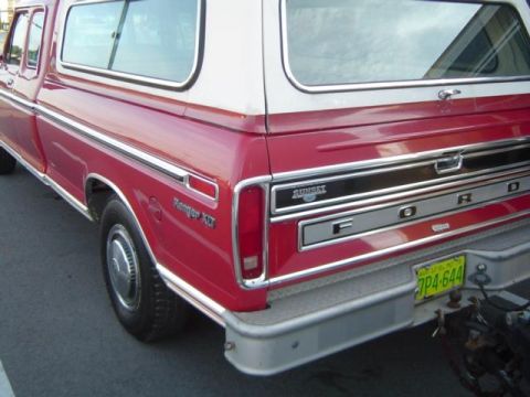 1979 Ford Bronco - Rear view of a red Ford pickup truck with a white camper shell, chrome trim and a yellow license plate.