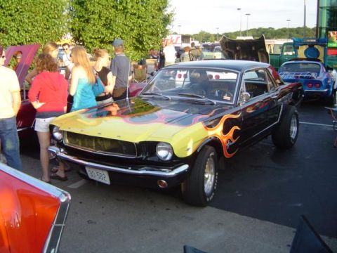 1979 Ford Bronco - A customized classic Mustang with flame graphics is displayed at a car show, with other vehicles and people around.