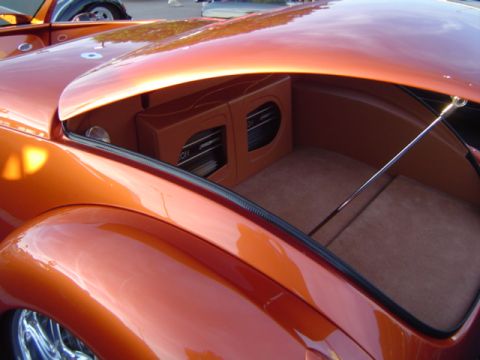 1979 Ford Bronco - The trunk of a custom orange car is open, revealing a carpeted interior with a dual subwoofer enclosure.
