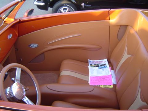 1979 Ford Bronco - Interior view of a custom orange convertible, tan upholstery and papers on the passenger seat. Another vehicle is visible in the background.