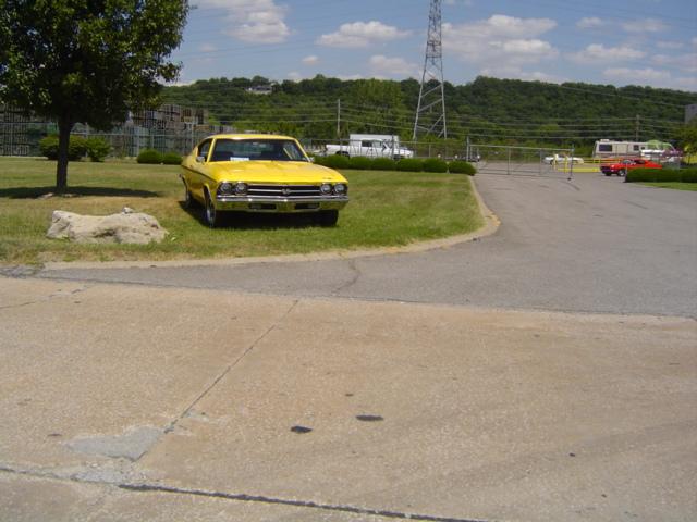 Yellow 1969 Chevrolet Chevelle parked on grass, front view. Other vehicles and a power line tower are in the background