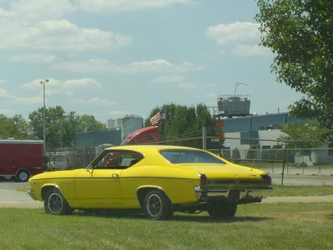1979 Ford Bronco - A bright yellow coupe, likely a 1969 model, sits on a grassy area with industrial buildings in the background.