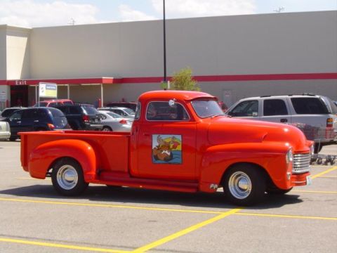 1979 Ford Bronco - A bright red pickup truck with a custom cartoon decal is parked in a lot outside a large building.