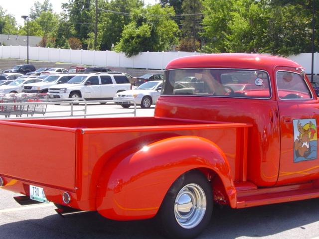 Red pickup truck with a cartoon moose graphic on the door, parked in a lot with other vehicles and shopping carts