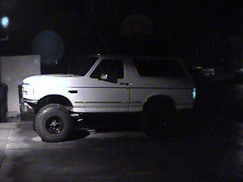 1994 Ford Bronco - A lifted white Ford Bronco is parked outdoors at night, showing its side profile.