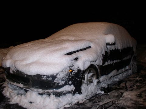 1996 Ford Probe - A black car is completely covered in snow, with only parts of the headlights and wheels visible.
