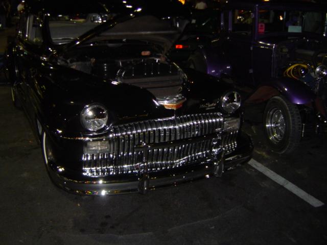 Black sedan with chrome grille and hood open, parked next to a purple car
