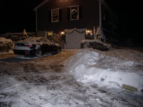 1996 Ford Probe - A black car is parked in a driveway covered in snow, with a house in the background decorated for the holidays.