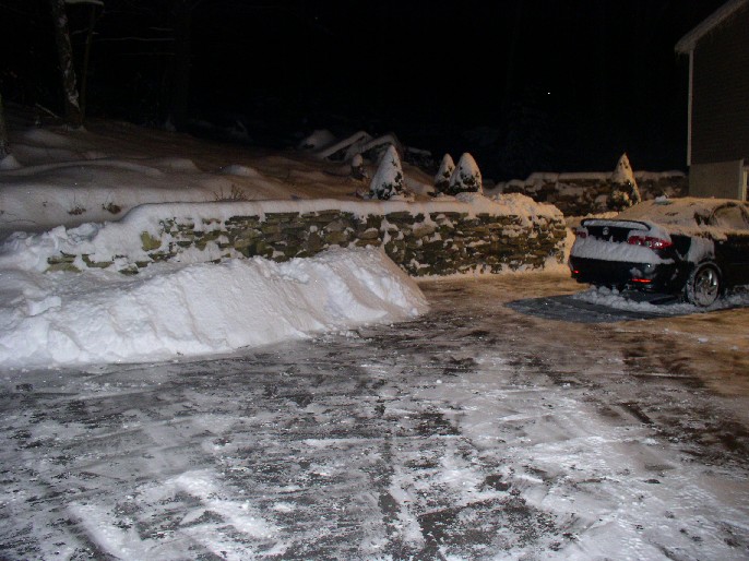 Black car with a spoiler parked in a snowy driveway at night