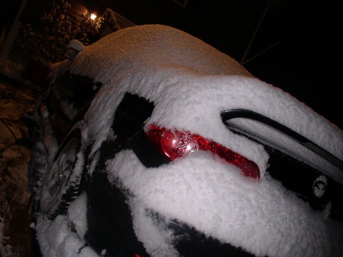 car covered in snow at night, showing a taillight