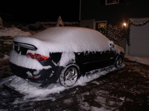 1996 Ford Probe - A black car is parked on a driveway, heavily covered in snow during a winter night.