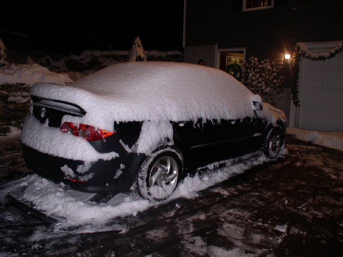 Black car covered in snow, parked on a driveway at night