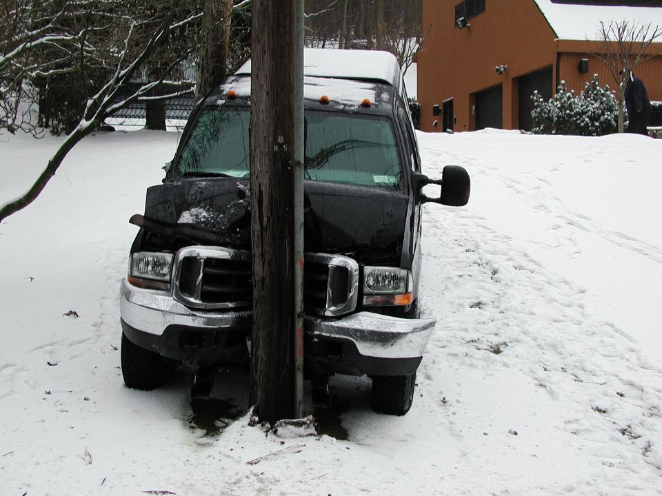 Black van front end smashed into a wooden utility pole in the snow