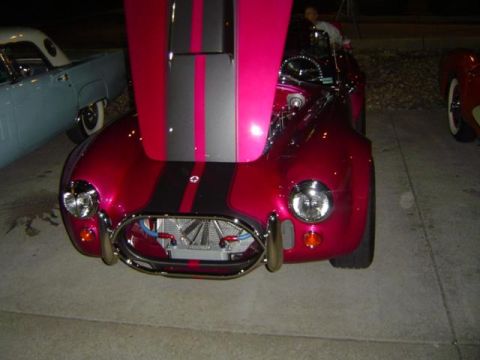 1979 Ford Bronco - A custom sports car with racing stripes is displayed with its hood open, parked alongside other vehicles.