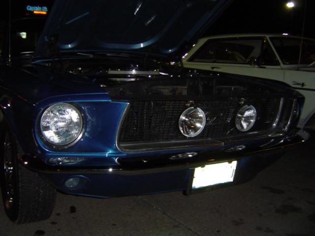 Front view of a blue 1967-1968 Ford Mustang with hood open, parked next to a white car