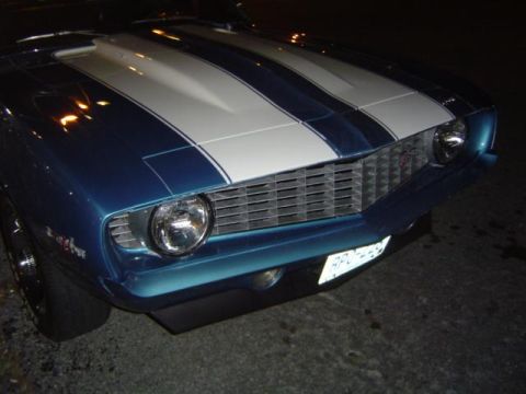 1979 Ford Bronco - A blue muscle car with white racing stripes is parked on asphalt at night.