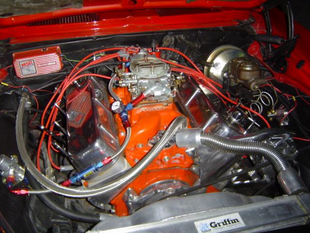 Close-up of a V8 engine in a red car's engine bay. Features an MSD ignition box and a Holley carburetor
