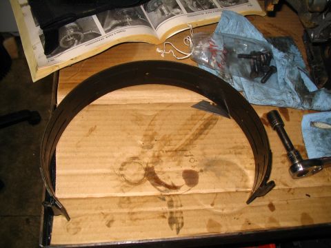1984 Ford Bronco - A transmission band, a bag of bolts, and a socket wrench are laid out on a table with a shop manual in the background.