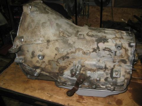 1984 Ford Bronco - A dirty automatic transmission is shown resting on a workbench in a garage.