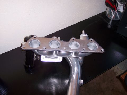 1999 Mitsubishi Mirage - A turbo exhaust manifold with four intake ports and a connected downpipe is shown on a black surface.