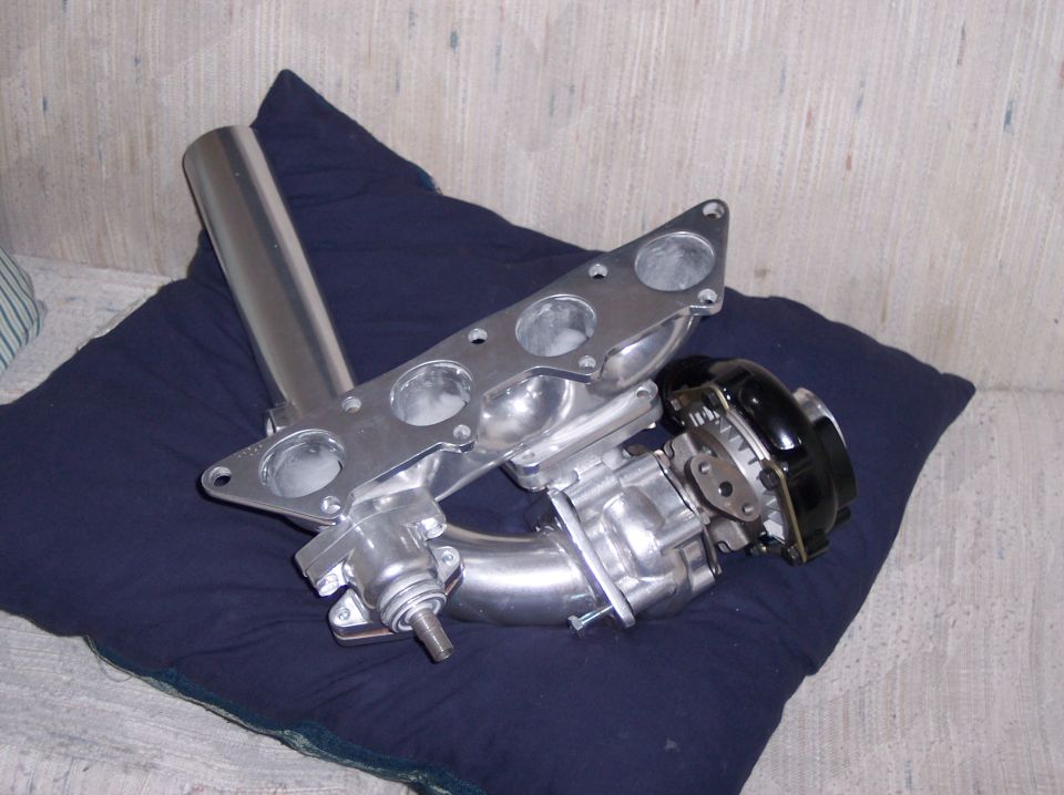 Aluminum four-cylinder intake manifold with throttle body on a blue cushion.
