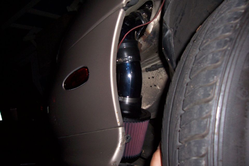close-up of aftermarket cold air intake with red filter next to tire and fender