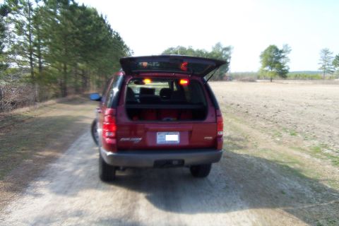 2005 Ford Explorer - Rear view of a red 2005 Ford Explorer with the trunk open, parked on a dirt road.