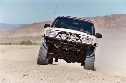 1985 Ford Bronco II - A white SUV navigates a dusty desert terrain, its tires angled as it turns.
