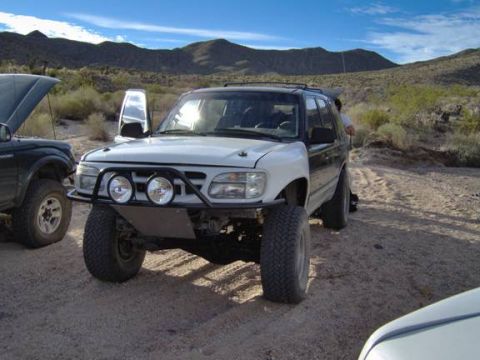 1985 Ford Bronco II - Two off-road vehicles are parked in a desert landscape under a blue sky.