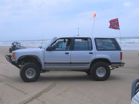 1985 Ford Bronco II - Silver SUV parked on a sandy beach with the ocean in the background and two flags flying.