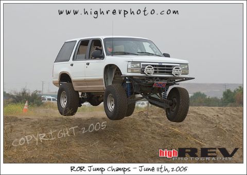 1985 Ford Bronco II - A modified white SUV is captured airborne during an off-road event, its suspension and large tires.