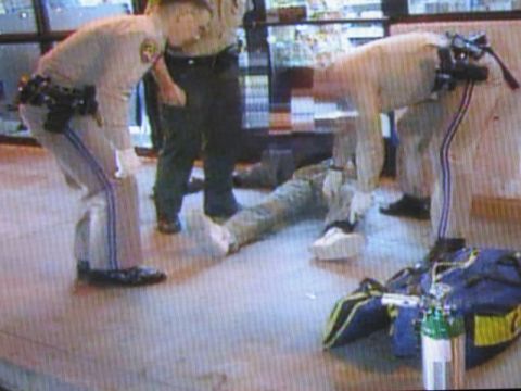 1991 Ford LTD Crown Victoria - photographed television frame showing uniformed officers in tan shirts attending to a person lying on a convenience-store floor.