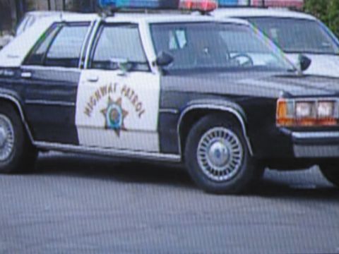 1991 Ford LTD Crown Victoria - photographed television frame showing the side of a black-and-white Highway Patrol sedan with roof lightbar and star door emblem.