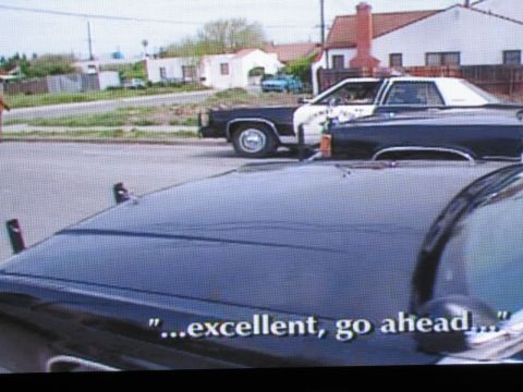 1991 Ford LTD Crown Victoria - photographed television frame of black-and-white patrol cars in a residential street, with subtitle reading excellent, go ahead.