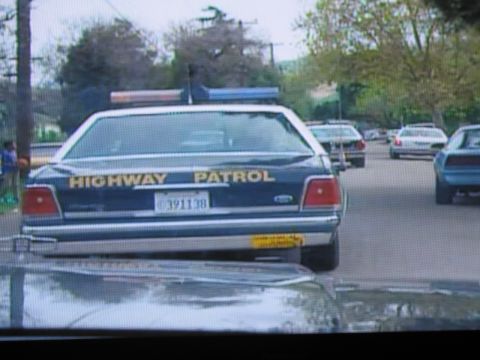 1991 Ford LTD Crown Victoria - photographed television frame showing the rear of a dark Highway Patrol sedan with yellow HIGHWAY PATROL lettering and lightbar.