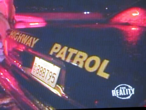 1991 Ford LTD Crown Victoria - photographed nighttime television frame of a patrol car's rear lit red, showing yellow HIGHWAY PATROL lettering and a Fox Reality logo.